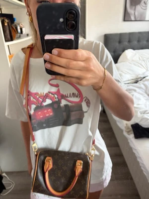 Louis Vuitton Monogram handväska - Säljer en klassisk Louis Vuitton handväska i brunt monogrammönster med beige och guldiga detaljer. Väskan har både handtag och justerbar axelrem i läder samt guldfärgade metalldetaljer. Perfekt storlek för det viktigaste och en ikonisk accessoar.