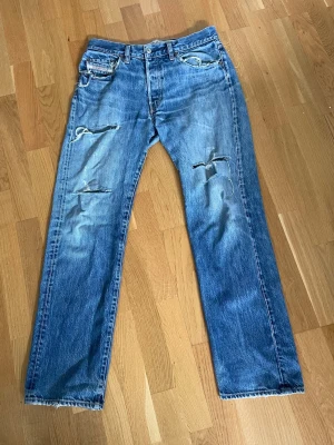 Blå slitna jeans från Diesel Y2K - Står w33 men sitter som w32. Säljer ett par blå jeans från Diesel med raka ben och flera slitningar och hål på framsidan. Jeansen har klassisk femficksdesign och tydlig vintagekänsla. Materialet är denim i bomull och färgen är tvättad blå med ljusare partier.