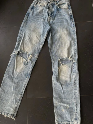 Ljusblå slitna jeans - Säljer ett par ljusblå jeans från Ginatricot med raka ben och stora slitningar över båda knäna.