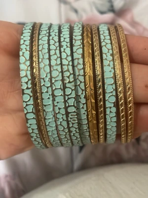 Set med turkosa och guldiga armband - Säljer ett set med flera smala armband i turkos och guld. Armbanden har ett mönster av små turkosa stenar och detaljerade guldkanter med graverade mönster. Perfekt för att skapa en färgstark och unik look.