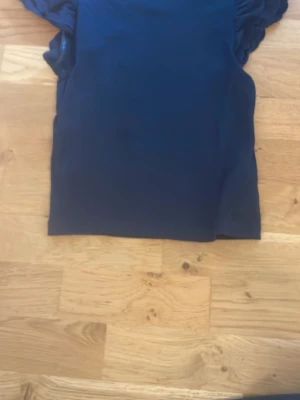 Mörkblå topp med puffärmar - Snygg mörkblå topp med puffiga korta ärmar och rund halsringning. Perfekt för dig som vill ha en enkel men ändå trendig look. Materialet känns mjukt och stretchigt, troligen bomull eller polyester.