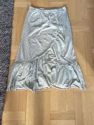 Ljusblå blommig med volang - Säljer en ljusblå med små blommor och volangkant. Kjolen har en mjuk och flowy känsla, perfekt för dig som gillar romantisk stil. Passar till både sneakers och sandaler.