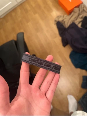 Grått Christian Dior J'Adior armband - Snyggt grått armband från Christian Dior med texten 'J'Adior' invävd. Tillverkat i textil med en stilren och modern look. Perfekt accessoar för dig som gillar exklusiva märken och vill addera en cool detalj till din outfit. Helt ny oanvänd! Priset kan diskuteras vid snabbaffär!!
