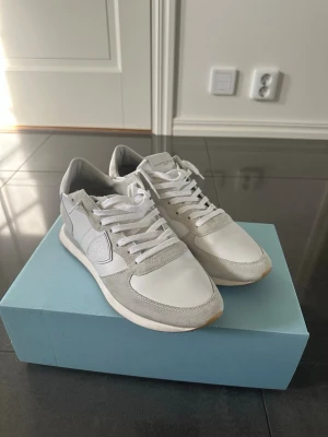Vita sneakers från Philippe Model - Snygga vita sneakers från Philippe Model med detaljer i mocka och läder. Klassisk låg modell med vita snören och gummisula. Diskret logga på sidan och tungan. Perfekta för en clean och stilren look.
