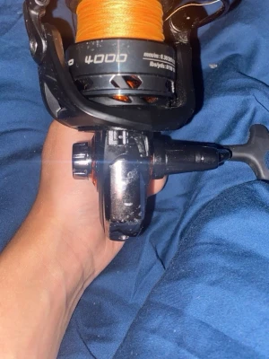 Svart fiskerulle Fire Wave 4000 - Fiskerulle Fire Wave 4000 i svart med orange fiskelina. Handtaget är avtagbart och rullen har detaljer i metall och plast. Perfekt för dig som gillar fiske och vill ha en pålitlig rulle till spöet.