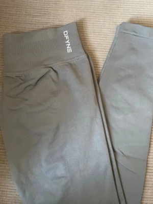 Gråa seamless leggings från DFYNE - Snygga gråa seamless leggings från DFYNE med hög midja och ribbad linning. Stretchigt material som sitter skönt och formar sig efter kroppen. Perfekta för träning eller chill. Diskret logga vid midjan för en clean look.