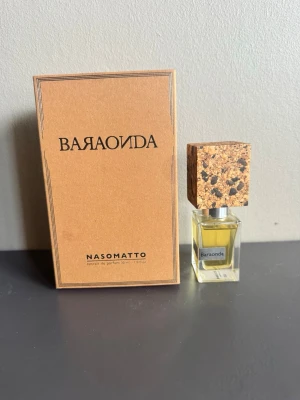 Nasomatto Baraonda parfym 30ml - Unik parfym från Nasomatto, Baraonda, i en elegant glasflaska med fyrkantigt korklock i korkmaterial. Doften kommer i en stilren brun kartong med svart text. Flaskan rymmer 30 ml extrakt de parfum och har en modern, minimalistisk design.