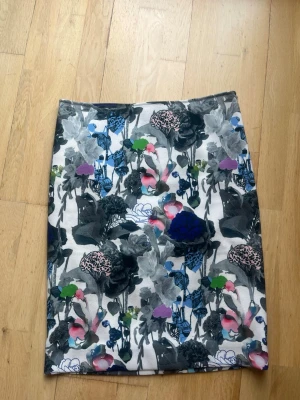 Blommig mellanlång kjol från COS - Säljer en snygg blommig kjol från COS med färgstarkt mönster i svart, grått, blått, rosa, grönt och lila. Kjolen har rak passform och är i ett mjukt bomullsmaterial. Perfekt för dig som vill sticka ut lite extra!