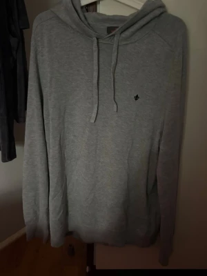 Grå hoodie med broderad logga - En stilren grå hoodie med huva och dragsnören. Tröjan har en liten svart broderad logga på bröstet och är tillverkad i ett mjukt, bekvämt material. Perfekt för en avslappnad look och enkel att matcha med andra plagg. Den är aldrig använd svin skön. Priset kan diskuteras vid snabb affär. Den passar L och M.