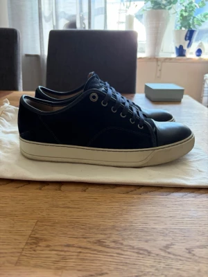Svarta sneakers i mocka och läder - Snygga svarta sneakers med ovandel i mocka och tåparti i slätt läder. Skorna har vita sulor och svarta skosnören. Perfekta för dig som gillar stilrena och klassiska sneakers med en modern touch.