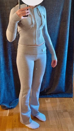 Beige stickad ziptröja med byxor - Beige stickad hoodie + byxor. Hoodien har dragkedja framtill och dragsko i huvan. Tröjan har bred ribbstickning i midjan och vid ärmsluten, samt långa ärmar och figurnära passform. Materialet är mjukt och stretchigt. Aldrig använt! Fått i present så vet tyvärr inte märket.