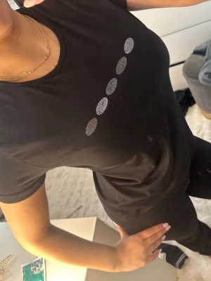 Svart t-shirt med silverprickar - Snygg svart t-shirt med rund hals och fem silverfärgade prickar i rad på bröstet. T-shirten har en klassisk passform och är tillverkad i mjukt bomullsmaterial. Perfekt för en stilren och enkel look. Trycket har försvunnit lite