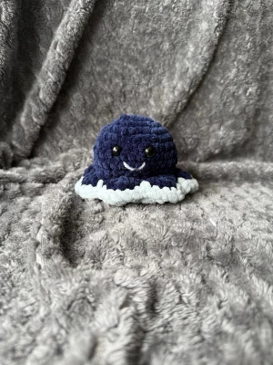 Vändbar virkad bläckfisk plushie - Söt handvirkad vändbar bläckfisk plushie i mjuk sammet. Ena sidan är mörkblå med vitt leende och svarta ögon, andra sidan är ljusblå med svart mun och svarta ögon. Perfekt som dekoration eller present.