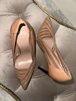 Zara Beige klackar - Säljer ett par snygga beige klackar från Zara i storlek 38. Skorna har spetsig tå, höga smala klackar och coola meshdetaljer i sidorna som ger en modern vibe. Perfekta för dig som vill sticka ut lite extra med dina skor. 