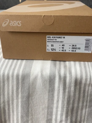 ASICS Gel-Kayano 14 White/Graphite - Säljer ett par ASICS Gel-Kayano 14 sneakers i färgen vit och graphite grey. Skorna har en sportig siluett med mesh och syntetmaterial, samt klassiska ASICS-stripes på sidorna. Sulan är robust och designad för komfort och stil. Perfekta för dig som gillar retrovibbar och streetwear.