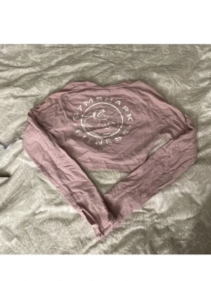 Rosa croppad långärmad topp Gymshark - Säljer en rosa croppad långärmad topp från Gymshark med stort vitt tryck på bröstet. Perfekt för träning eller chill, med skön passform och mjukt material. Snygg och enkel att matcha med tights eller jeans✨