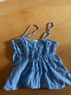 Blåvit randig linnetopp med smala band - Söt blå och vit randig linnetopp med smala axelband och resår i midjan. Perfekt för varma dagar och enkel att matcha med jeans eller shorts. Luftigt material och avslappnad passform.
