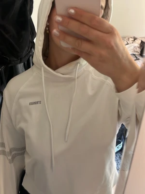 Vit hoodie från Stronger, mycket bra skick - Säljer en vit hoodie från Stronger med huva och dragsko. Hoodien har tryckt logga på bröstet och diskreta detaljer på ärmen. Perfekt för en sportig och avslappnad stil.