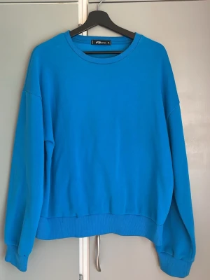 Blå sweatshirt från FB Sister - En enkel och stilren blå sweatshirt från FB Sister. Tröjan har rund halsringning, ribbade muddar vid ärmslut och nederkant samt en avslappnad passform. Perfekt för en chill och casual look. Materialet känns mjukt och bekvämt mot huden. Passar om man brukar ha M/L