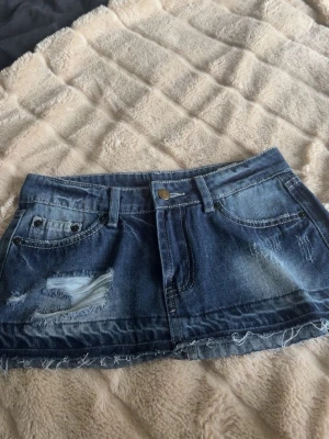 Blå jeanskjol med slitningar  - Säljer en blå jeanskjol i klassisk denim med två bakfickor , fransig kant nedtill.  och en snygg tvättad look som ger en avslappnad vibe. Perfekt till sneakers eller boots.