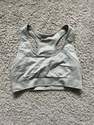 Ljusgrå sport-bh - Snygg ljusgrå sport-bh med brottarrygg och bred resår under bysten. Tillverkad i ett stretchigt och mjukt material som andas, perfekt för träning eller gym. Diskret mönstrad struktur på sidorna för extra stil.