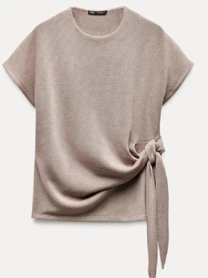 Beige topp med knyt från Zara - Trendig beige topp från Zara med rund halsringning och korta ärmar. Toppen har en snygg knytdetalj i sidan som ger en unik look. Perfekt att styla med både jeans och kjol för en avslappnad men chic outfit.