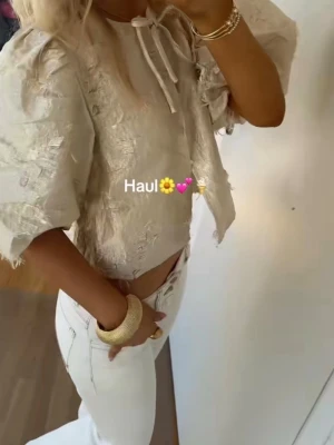 NAKD, Beige croppad blus med puffärm - Trendig beige croppad blus med puffiga korta ärmar och knytband vid halsen. Materialet har en strukturerad, lite glansig finish och ger en lyxig känsla. Den är endast använd ett fåtal gånger och är i ny skick💕