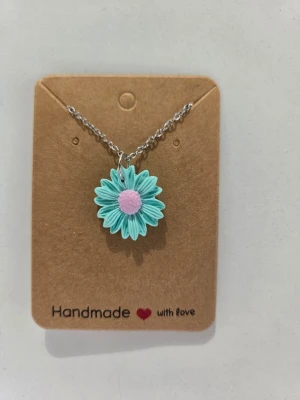 Handgjort halsband med turkos blomma - Sött halsband med en handgjord blomma i turkos och ljusrosa. Blomman sitter på en tunn silverfärgad kedja, reglerbar upp till 45 cm. Perfekt för sommaren! Hslsbandet är gjort för hand av mig i polymerlera. 