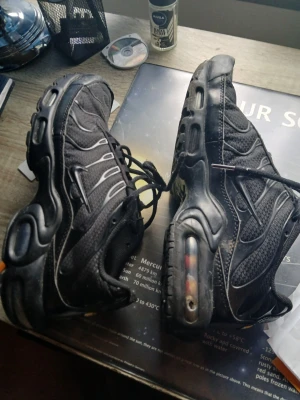 Nike Air Max Plus svarta sneakers - Säljer ett par helsvarta Nike Air Max Plus sneakers med klassisk TN-logga på hälen. Skorna har mesh- och syntetmaterial, synlig Air-dämpning i sulan och vågiga detaljer längs sidorna. Perfekta för dig som gillar streetwear och sportig stil. Det är ett hål  i skor men den går använd och det finns inga sulor. Skorna är har slitage men det går använda dom.