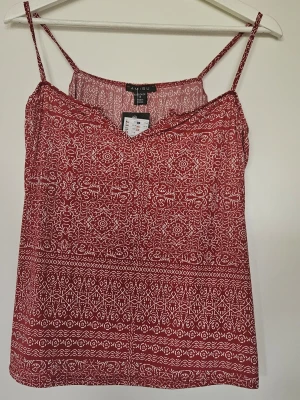 Röd mönstrad linnetopp från Amisu - Snygg röd linnetopp från Amisu med vitt mönster och tunna axelband. Toppen har en avslappnad passform och är perfekt för varma dagar. Tillverkad i polyester som känns skön mot huden. Supersnygg till jeans eller shorts! Ny med prislapp.