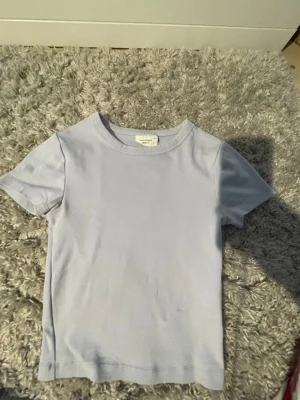 Ljusblå basic t-shirt från Gina  - Jätte söt ljusblå tight tröja från Gina Tricot i mjuk bomull. Modellen är klassisk med rund halsringning och korta ärmar. Perfekt att matcha med jeans eller shorts.
