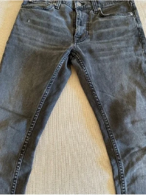 Nudie jeans w27 l28 - Säljer ett par svarta jeans från Nudie Jeans med klassisk femficksdesign och svarta broderade detaljer på bakfickorna. Jeansen har normal passform och raka ben, tillverkade i mjuk bomullsdenim. Perfekta för dig som gillar stilrena och tidlösa jeans. Anledningen till försäljningen är för att dom helt enkelt inte passar längre. Modell lean Dean! W27 L28