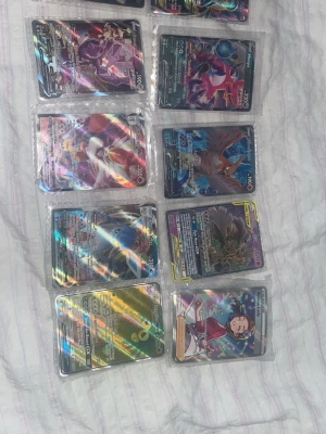 Pokémonkort samling holografiska - Säljer en samling Pokémonkort med holografisk effekt. Korten har färgstarka motiv och flera olika Pokémon och tränare. Alla korten ligger i plastfickor och har en glansig yta som reflekterar ljus. Perfekt för dig som vill utöka din samling eller gillar Pokémon!