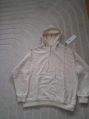 Ljusgrå hoodie från alo yoga - Snygg ljusgrå hoodie från alo med broderad logga på bröstet. Hoodien har en stor känguruficka framtill, dragsko i huvan och ribbade muddar vid ärmslut och nederkant. Perfekt för en chill och avslappnad stil.