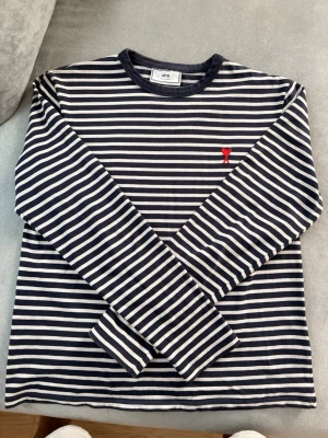 Ami Paris randning långärmad tröja - Säljer en klassisk randig topp från Ami Paris med marinblå och vita ränder samt ett rött broderat hjärta på bröstet.