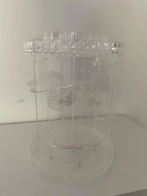 Roterande sminkorganizer i akryl - Transparent roterande sminkorganizer i akryl med flera hyllplan och fack för förvaring av smink, borstar eller andra skönhetsprodukter. Rund form med dekorativ kant upptill och nertill. Perfekt för att hålla ordning på ditt sminkbord.