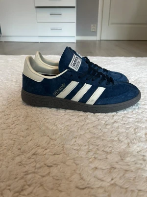 Adidas Spezial blå sneakers - Adidas Spezial sneakers i blå mocka med vita detaljer och klassiska tre ränder på sidorna. Skorna har lågt skaft, svart sula och vit hälkappa. Perfekta för dig som gillar retrostil och streetwear.