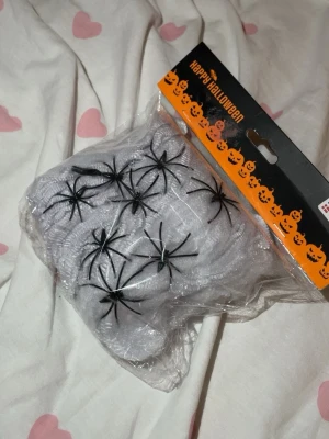 Halloween spindelnät med plastspindlar - Ett paket med vitt spindelnät och svarta plastspindlar, perfekt för att dekorera till Halloween eller maskerad. Nätet är stretchigt och lätt att forma, och spindlarna ger en läskig effekt. Kommer i originalförpackning.
