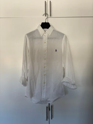 Vit linneskjorta från Ralph Lauren - Säljer en vit linneskjorta från Ralph Lauren i storlek XS (slim fit). Skjortan är i fint skick och sparsamt använd.  Perfekt till både sommar och mer uppklädda tillfällen – lätt och stilren. Nypris ligger högt, så detta är ett bra kap! Skick: Mycket bra  Hör av dig vid frågor eller om du vill ha fler bilder!