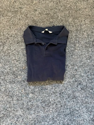 Marinblå pikétröja från William & Sons - Klassisk marinblå pikétröja från William & Sons med krage, korta ärmar och knappar framtill. Tillverkad i mjuk bomull för en bekväm känsla och stilren look.