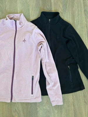 Rosa och svart fleecetröja från Cross Sportswear - Två fleecetröjor från Tuxer, en rosa med lila dragkedjor och en i svart. Perfekta för lager-på-lager och outdooraktiviteter. Den svarta är nopprig, se bild. Djur och rökfritt hem.