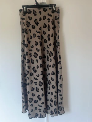 Beige långkjol med leopardmönster - Snygg beige långkjol med trendigt leopardmönster. Kjolen har en rak och flowy passform som ger en cool och avslappnad look. Perfekt att styla med en enkel topp eller stickad tröja. Materialet känns lätt och skönt mot huden.