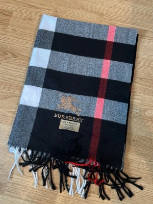 Burberry rutig halsduk svart - Snygg halsduk från Burberry i klassiskt rutigt mönster med svart, grått, vitt och röda detaljer. 