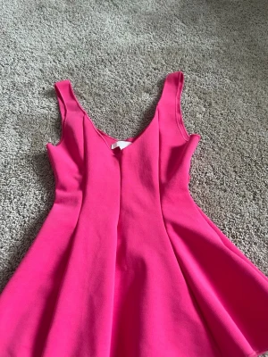 Rosa ärmlös topp med v-ringning - Snygg rosa topp med v-ringad hals och ärmlös design. Toppen har en utställd form som ger en feminin siluett. Perfekt för dig som vill sticka ut med färg och enkel stil.