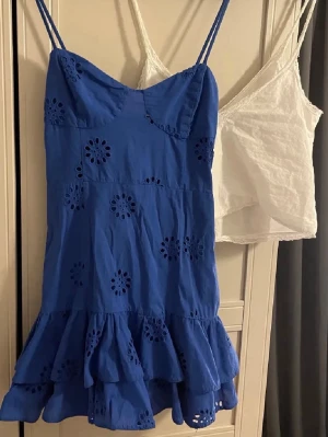 Blå klänning från Zara  - Supersöt blå klänning med smala axelband och volang nertill. Klänningen har broderade blommor med hålmönster och är tillverkad i ett lätt bomullstyg. Perfekt för varma dagar och ger en fräsch look.