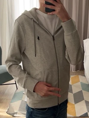 Polo Ralph Lauren grå ziphoodie - En skön grå Polo Ralph Lauren ziphoodie som är perfekt till sommaren som inte är nån tjock hoodie utan tunn som man kan matcha med en vit tröja under, officellt från Ralph Lauren EU hemsida, pris kan alltid diskuteras 