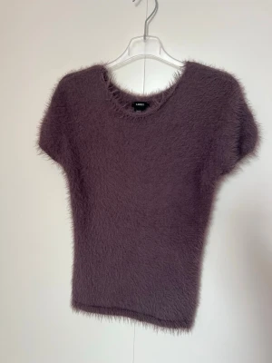 Lila fluffig stickad topp från Lindex i strl S,Helt ny! - Supermjuk och fluffig stickad topp i lila från Lindex. Modellen har korta ärmar, rund halsringning och en kroppsnära passform. Perfekt för dig som gillar trendiga och mysiga plagg med lite extra textur.