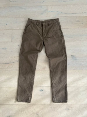 Grön bruna chinos från Massimo Dutti - Snygga bruna chinos från Massimo Dutti med klassisk passform och raka ben. Byxorna har två sidofickor fram och två bakfickor med knapp. Perfekta för en avslappnad men stilren look. Materialet är mjukt och bekvämt, troligtvis bomull. Priset går att diskutera.