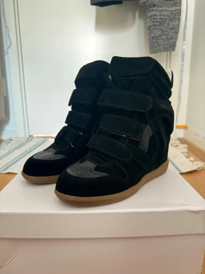 Svarta Isabel Marant - Snygga svarta wedge sneakers från Isabel Marant med kardborreband och gummisula. Skorna har en hög siluett och är tillverkade i mocka och läder. Perfekta för dig som vill ha en cool och trendig look med extra höjd.