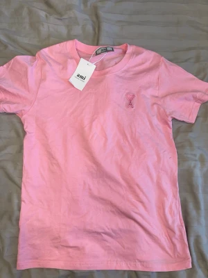 Rosa t-shirt från Ami Paris - Snygg rosa t-shirt från Ami Paris med broderad logga i form av ett hjärta på bröstet. Klassisk passform med korta ärmar och rund halsringning. Tillverkad i mjuk bomull som känns skön mot huden. Perfekt för en avslappnad och trendig look.